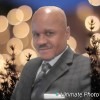 Dr. Dwight Webster, Sr. A man in a suit smiling at the camera with a blurred background of lights and trees.
